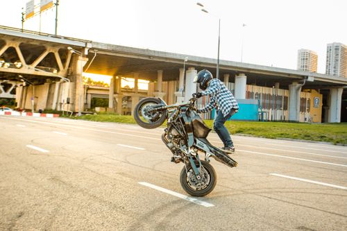 Free Motorcyclist performing a thrilling stunt on an empty city road near urban bridges. Stock Photo