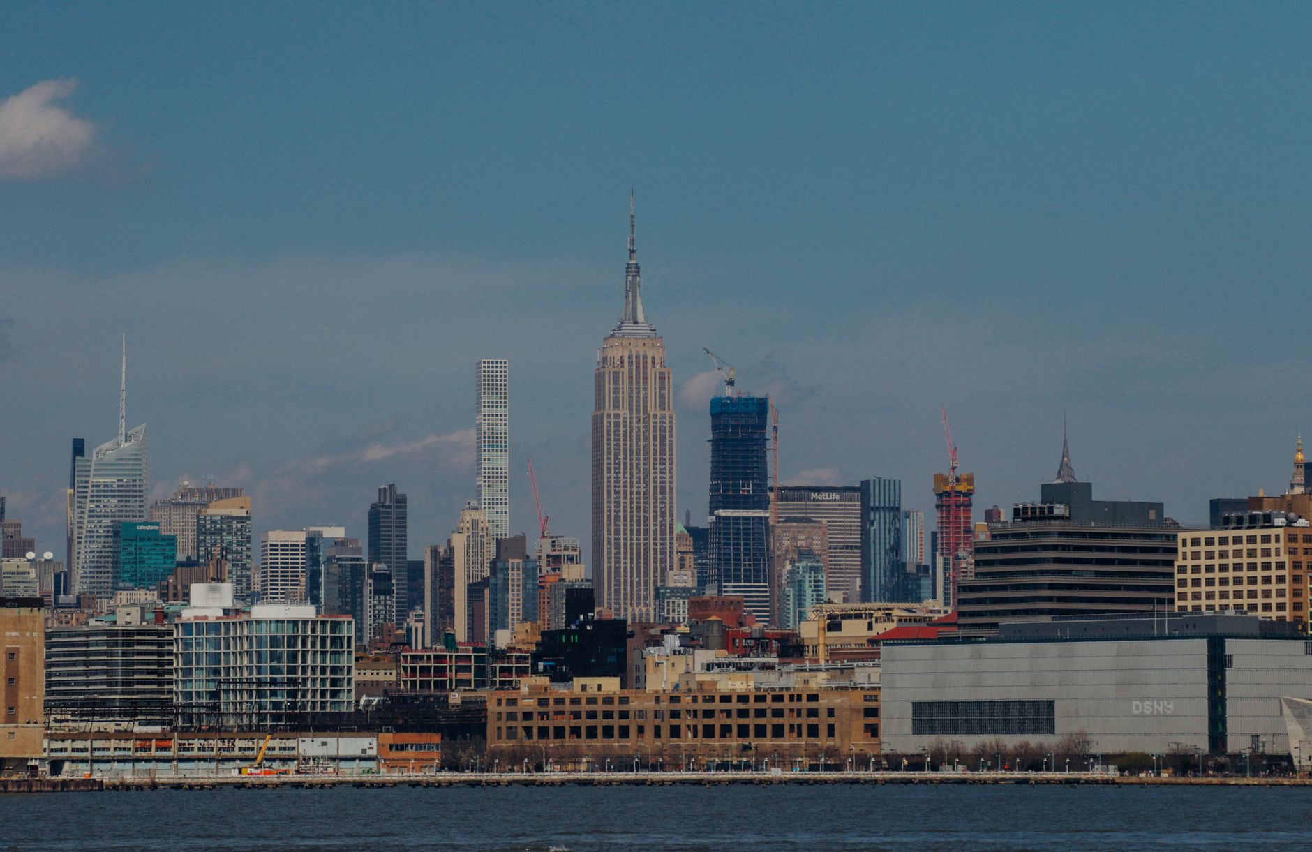 Iconic New York City skyline with the Empire State Building and surrounding skyscrapers under a clear blue sky.