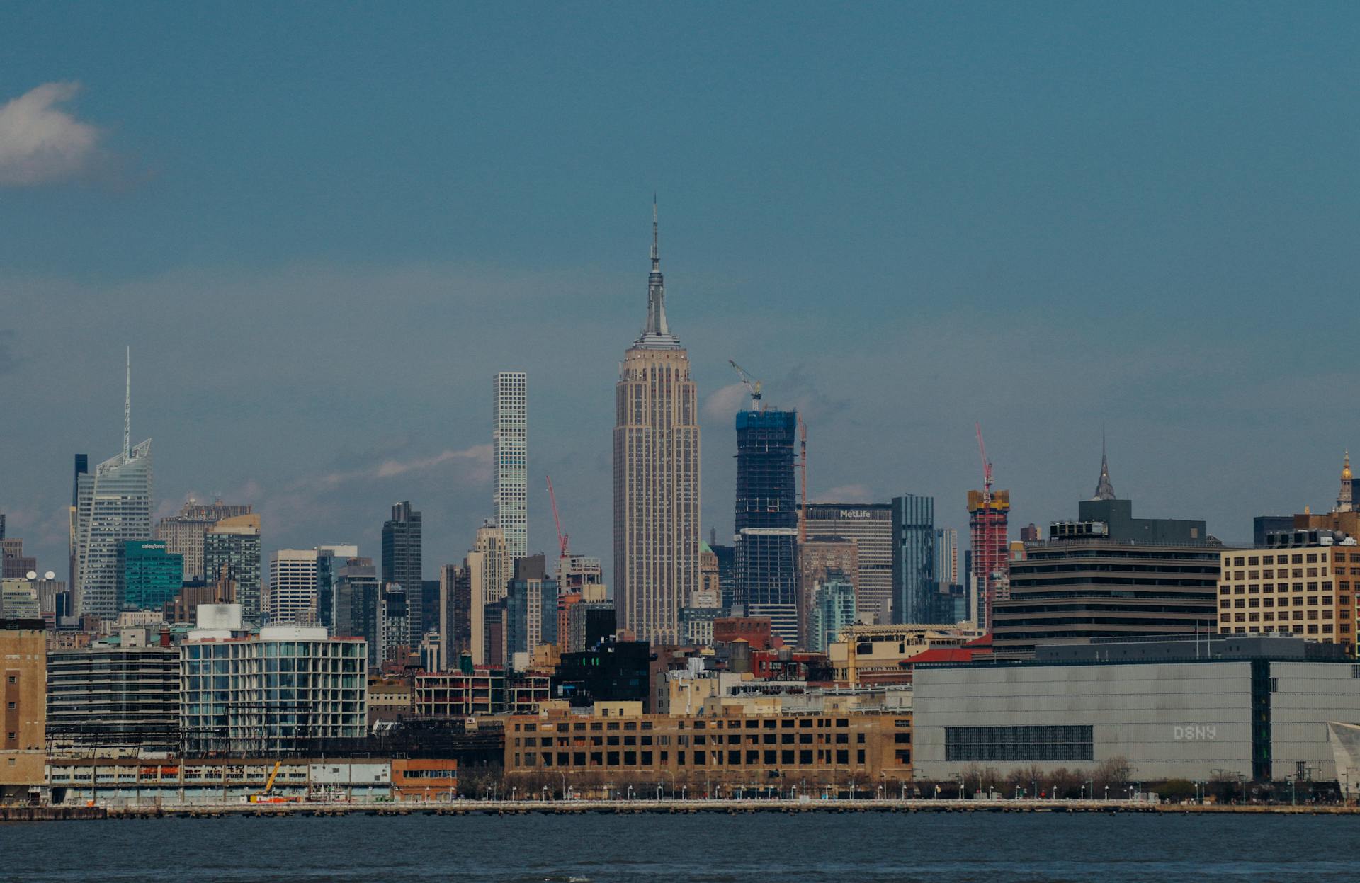 Iconic New York City skyline with the Empire State Building and surrounding skyscrapers under a clear blue sky.
