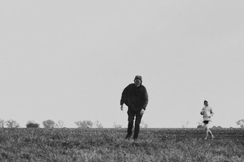 Black and White Photo of Two People Walking in a Field 