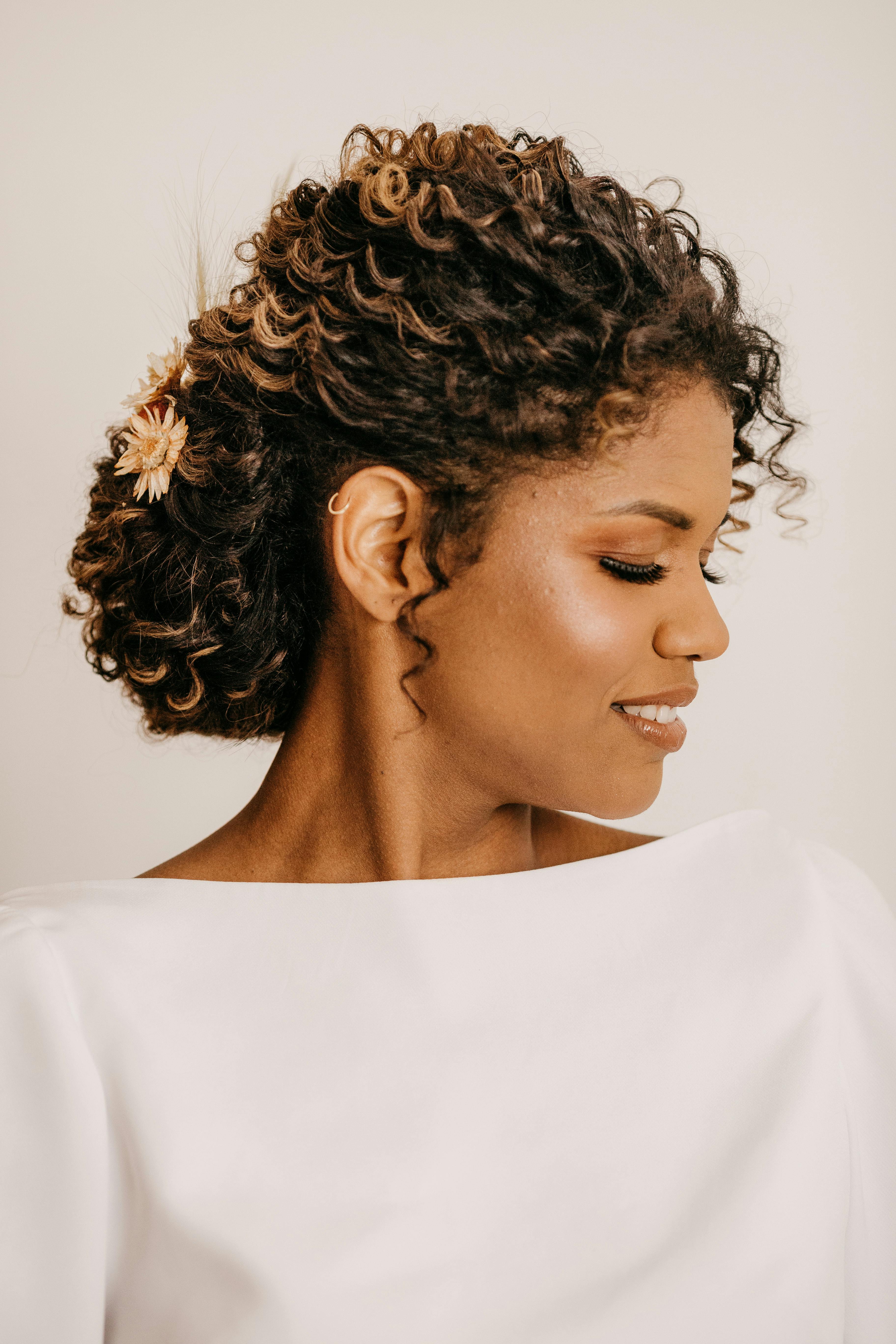 Beautiful portrait of an adult woman with curly hair, a flower accessory, and eyes closed in peaceful expression.