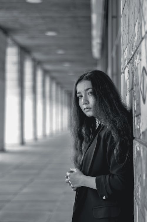 Young Woman with Long Black Hair Standing on Hallway in Grayscale Photography