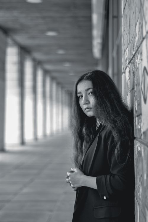 Free Black and white portrait of a young woman standing in a graffiti-lined hallway with soft lighting. Stock Photo