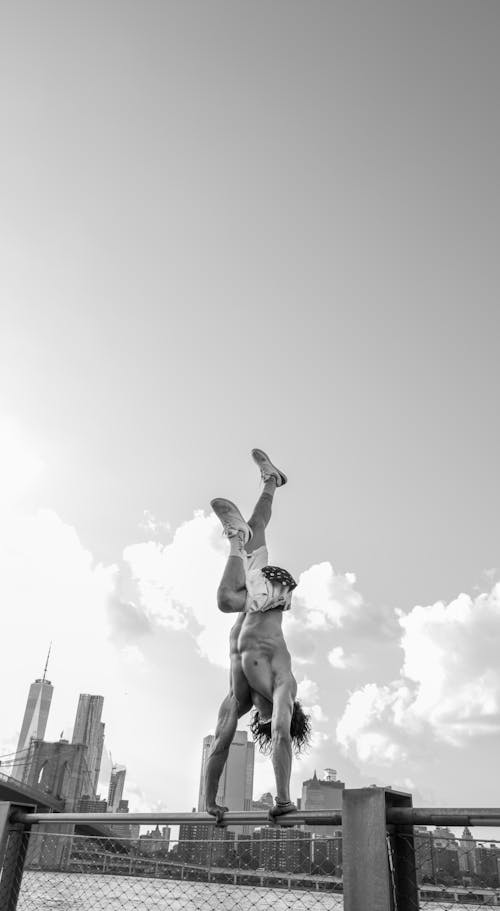 Black and White Photo of a Man Doing a Handstand on the Fence