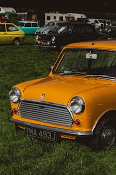 A vibrant yellow Mini Cooper parked among classic cars at an outdoor show.