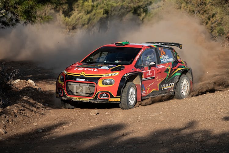 A Red Race Car Drifting On Dirt Road Emitting Dust