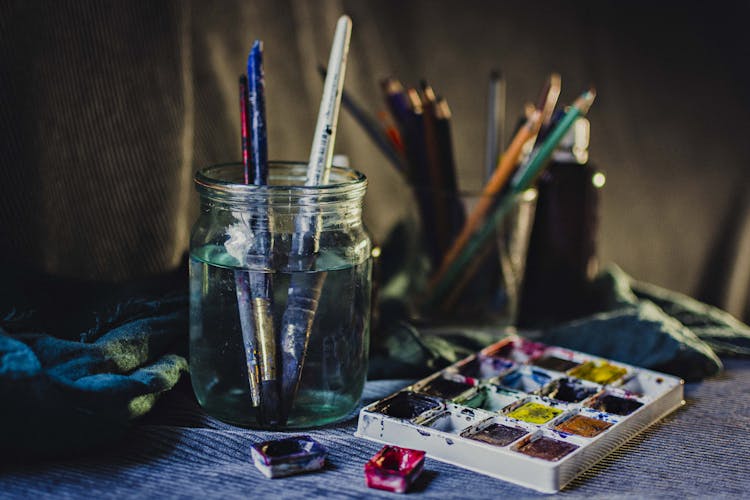 Watercolor Pallet Beside A Jar With Paint Brushes Soaked In Water