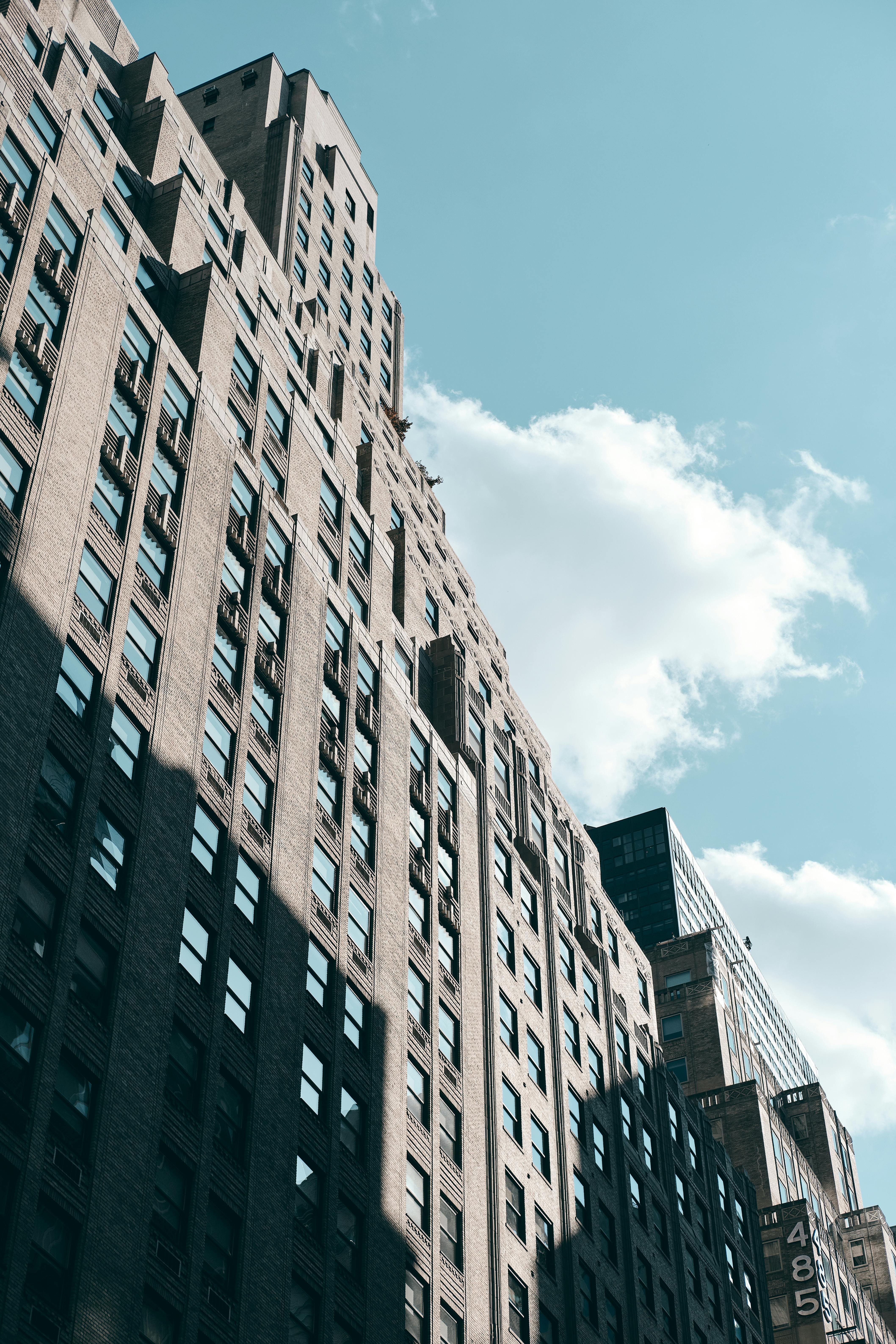 Low angle view of urban skyscrapers against a bright blue sky with clouds and shadows.
