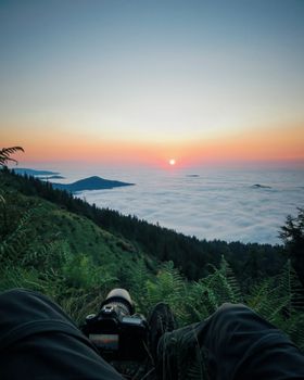 A photographer captures a serene sunrise over fog-covered mountains from a lush green vantage point.
