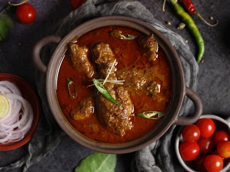 Aromatic Indian curry with meat and spices served in a traditional clay pot, garnished with chili.