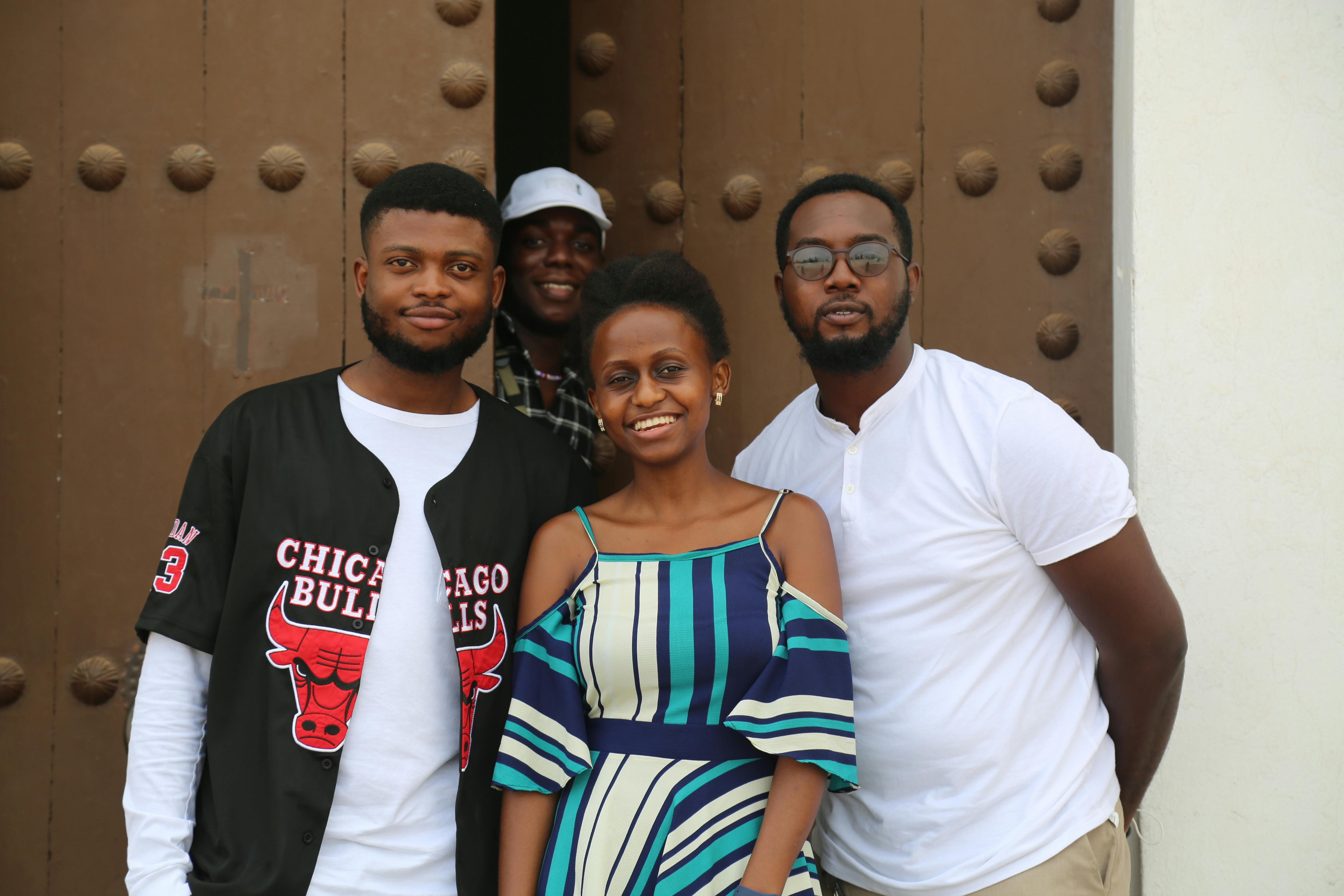A cheerful group of friends standing together, smiling in front of a large wooden door.