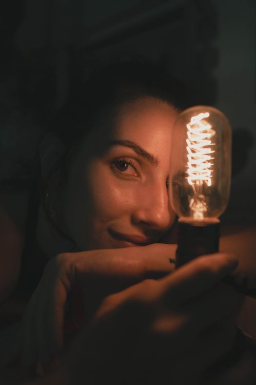 Free A captivating portrait of a woman holding a glowing lightbulb, creating a warm and moody ambiance. Stock Photo