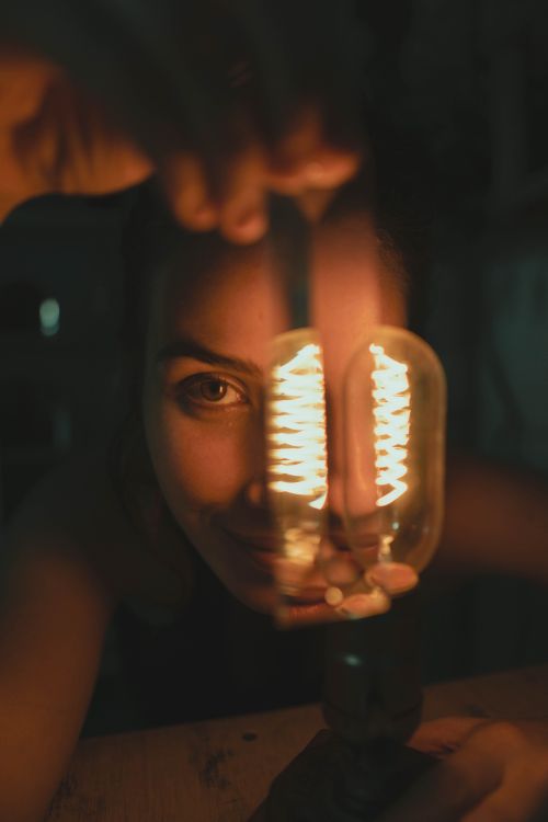 Free A woman peers through a glowing vintage light bulb, creating a warm, artistic effect. Stock Photo