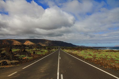 Concrete Road Between Mountain and Body of Water