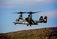 Black and Red Helicopter Flying over Brown Field