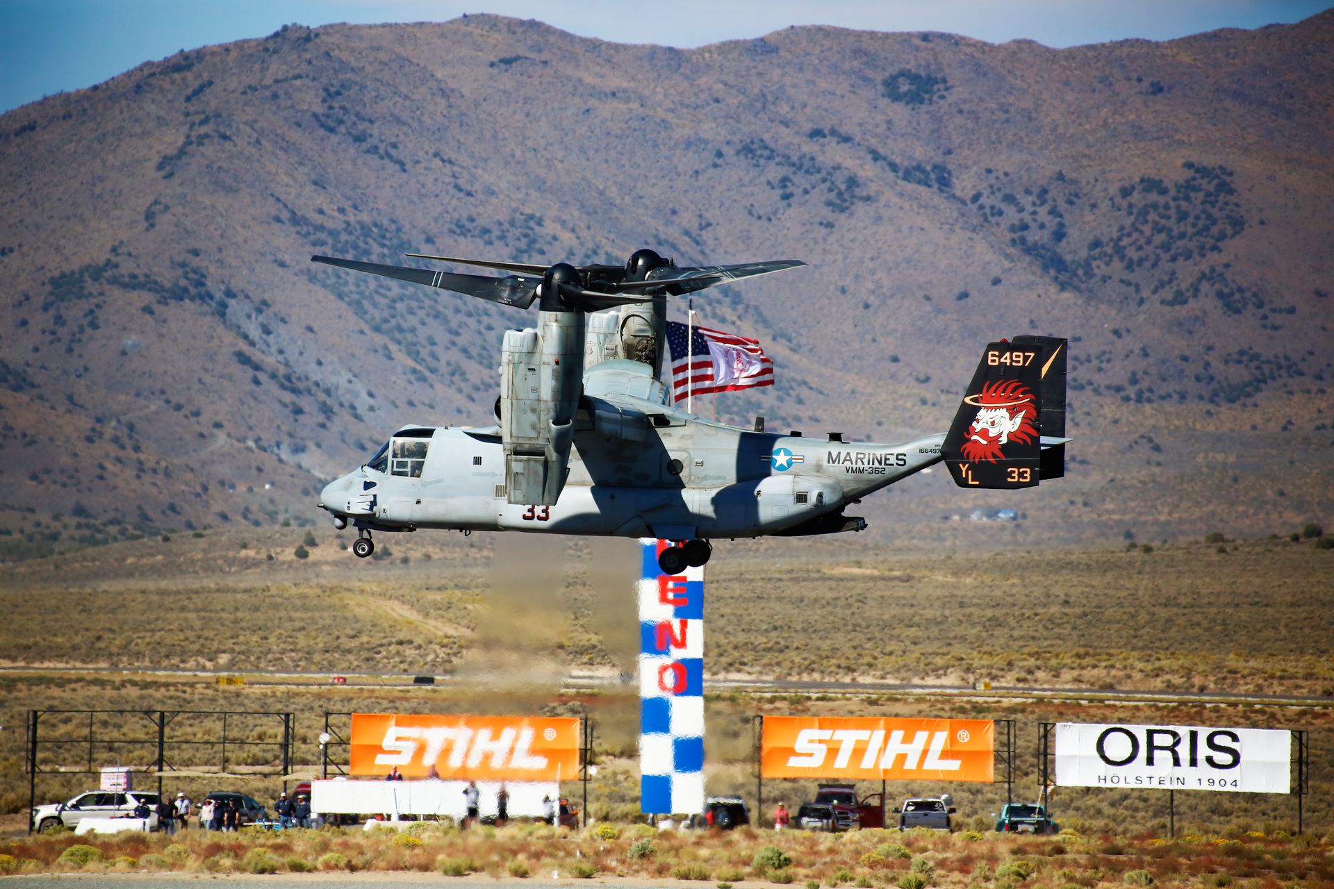 A modern aircraft in flight at the Reno Air Show with scenic mountains in the backdrop.