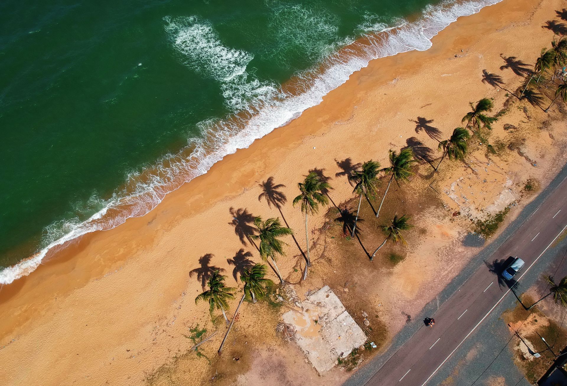 Stunning aerial view of a pristine beach in Paka, Terengganu, Malaysia with lush palm trees and waves.