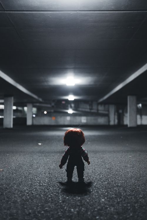 Free A creepy doll stands in silhouette under a dim light in an empty parking garage, creating a spooky atmosphere. Stock Photo
