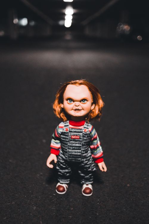 Free Eerie doll standing in a dimly lit street evokes horror vibes. Stock Photo