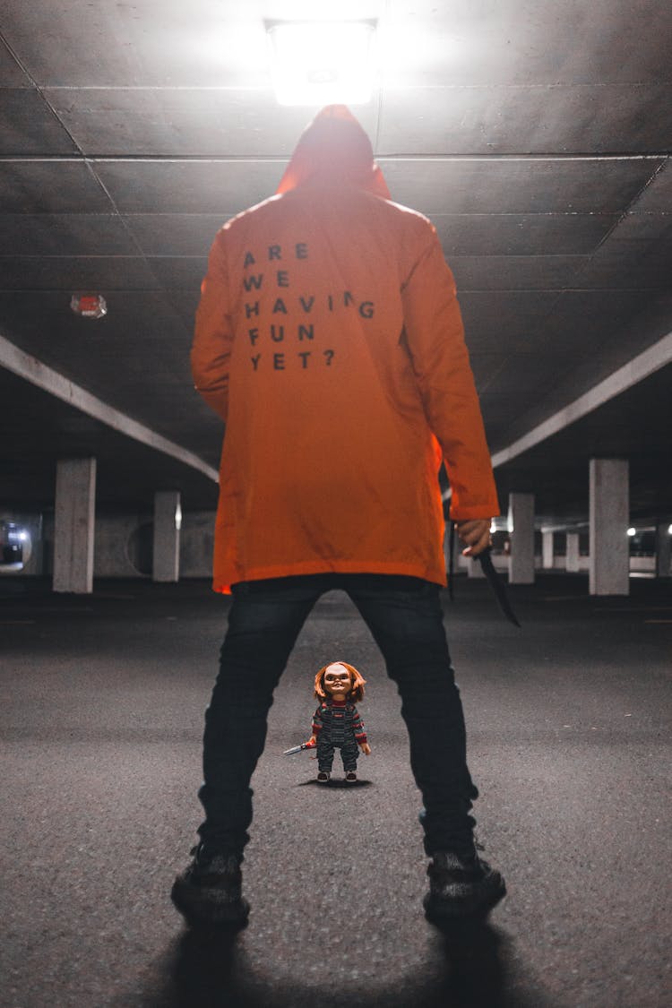 Man In An Orange Hoodie Brandishing A Knife Standing In Front Of A Doll 