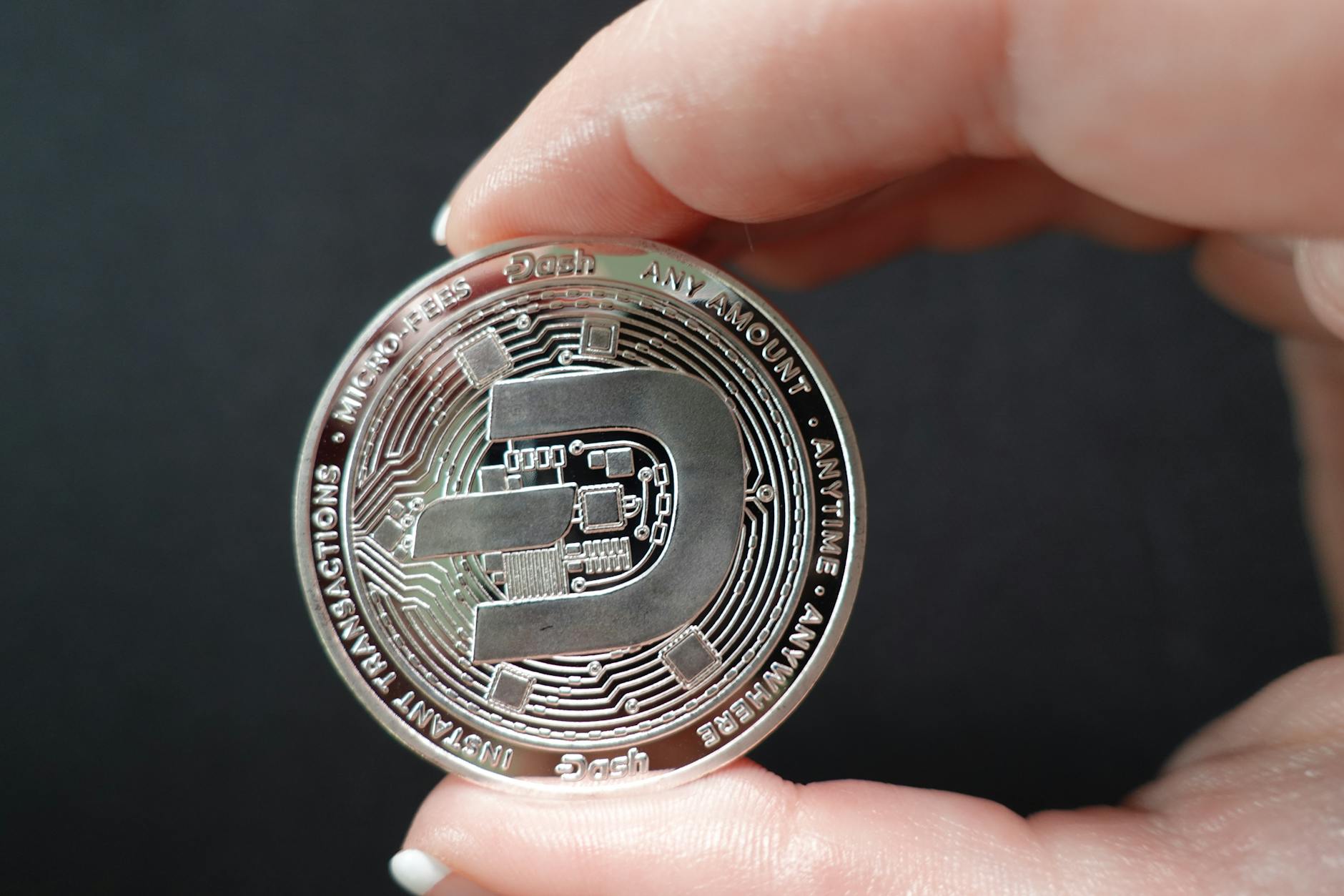 A close-up image showcasing a Dash coin held between fingers, emphasizing cryptocurrency and digital finance.