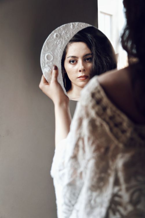 Free A woman gazes into a moon-shaped mirror, combining elegance with introspection. Stock Photo