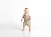 可爱的婴儿穿着米色工作服，站在白色背景下，展现着纯真和欢乐