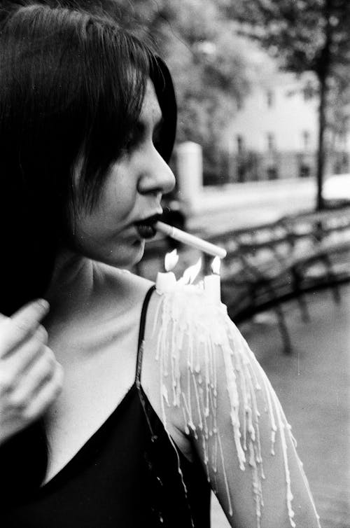 Black and White Photo of a Woman Lighting a Cigarette from Candles on Her Arm