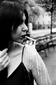 Spooky black and white portrait of a woman lighting a cigarette with candle wax in a surreal outdoor setting.
