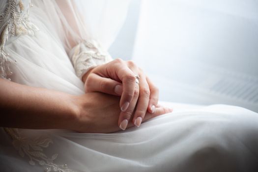 Close-up of a bride's hands in a delicate white gown, showcasing a wedding ring.