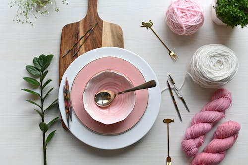 Arrangement of White and Pink Plates Cutlery and Wool Skeins