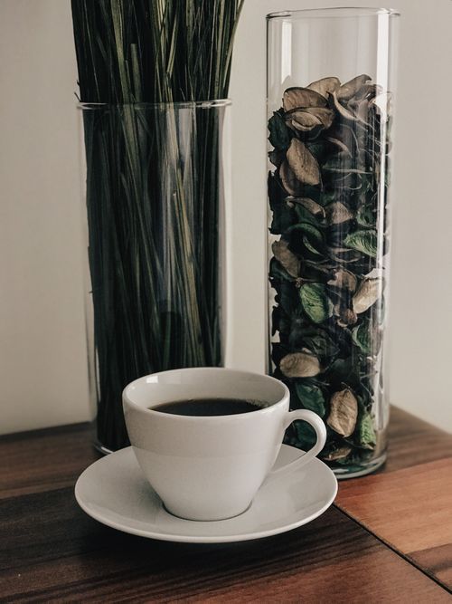 Free A minimalist scene featuring a cup of black coffee and decorative dried leaves on a wooden table. Stock Photo