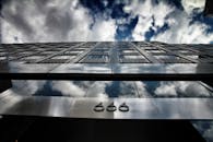 低角度视角下的现代建筑，外立面覆盖反光玻璃，映衬着醒目的云层