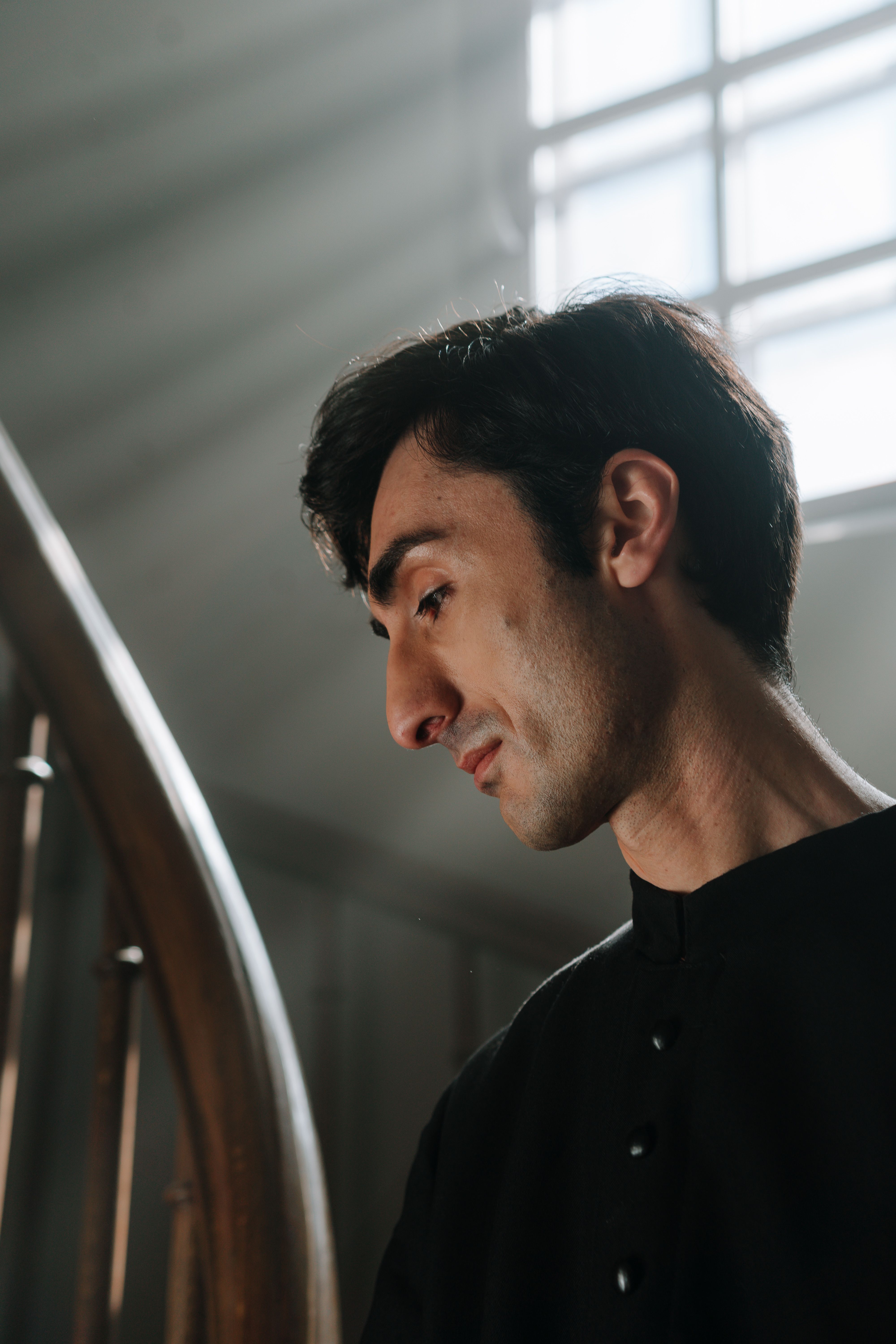 Thoughtful man gazes downwards, illuminated by soft ambient light near staircase.
