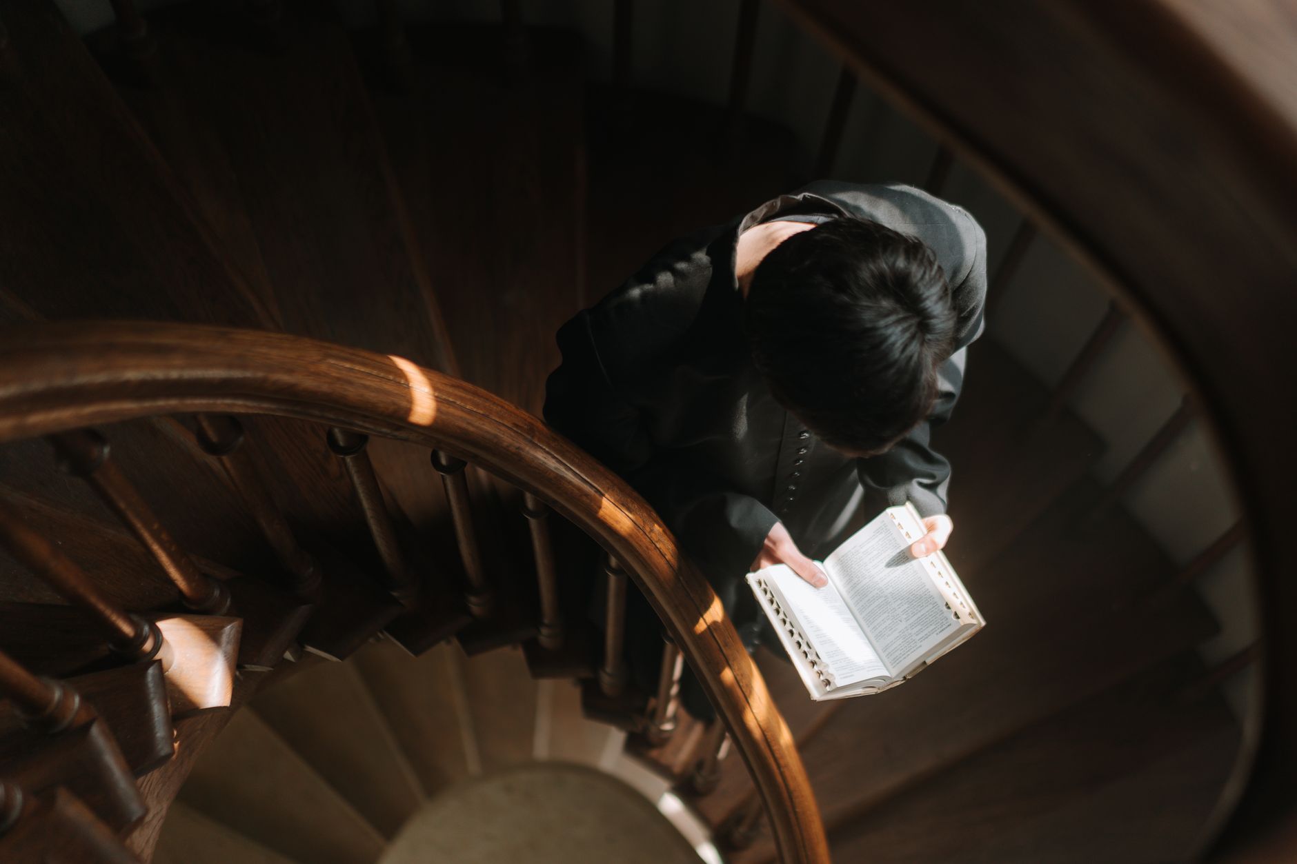 A priest reading from a holy book while standing on a spiral staircase, captured from above.