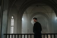 Man in Black Coat Standing Near White Window Curtain