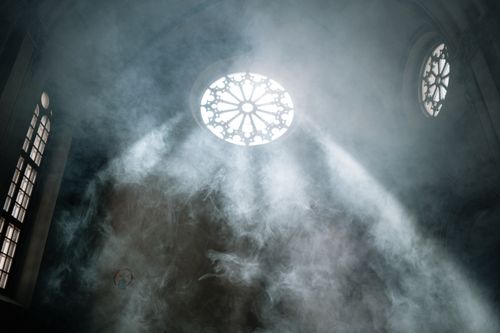 Free Sunlight streams through a church rosette window surrounded by smoky atmosphere, creating a mystical ambiance. Stock Photo
