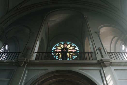 A priest stands at the altar in an ornate church with beautiful arches and stained glass.