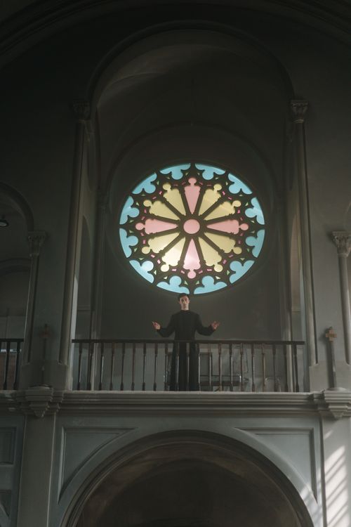 Free Priest stands in a church with a large stained glass window above. Stock Photo