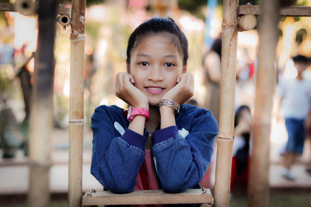 charming portrait of a young girl smiling framed by bamboo outdoors