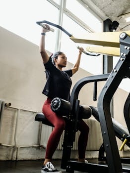 Asian woman working out on exercise machine, focusing on strength training in modern gym setting.
