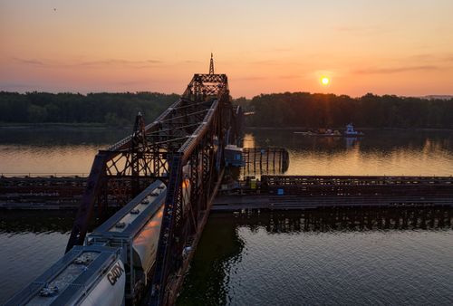 Free Aerial view of a rail bridge crossing a river in La Crescent, MN, during sunset, with calm waters and lush greenery. Stock Photo
