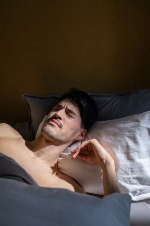 Free A man with eyes closed rests in bed, sunlight illuminating the room, creating a peaceful morning scene. Stock Photo