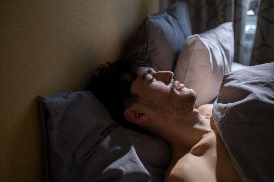 A man peacefully sleeping in bed with gentle morning light streaming in a cozy bedroom.