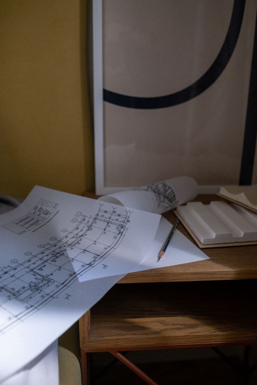 A close-up of architectural blueprints and pencil on a wooden desk in an office setting.