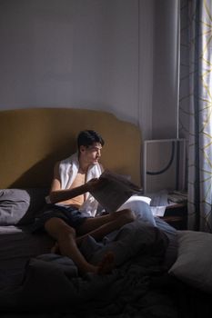 Man with towel reads newspaper in a dimly lit bedroom during the day, creating a relaxed and cozy atmosphere.