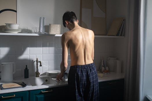 A shirtless man preparing breakfast in a modern kitchen during the early morning.