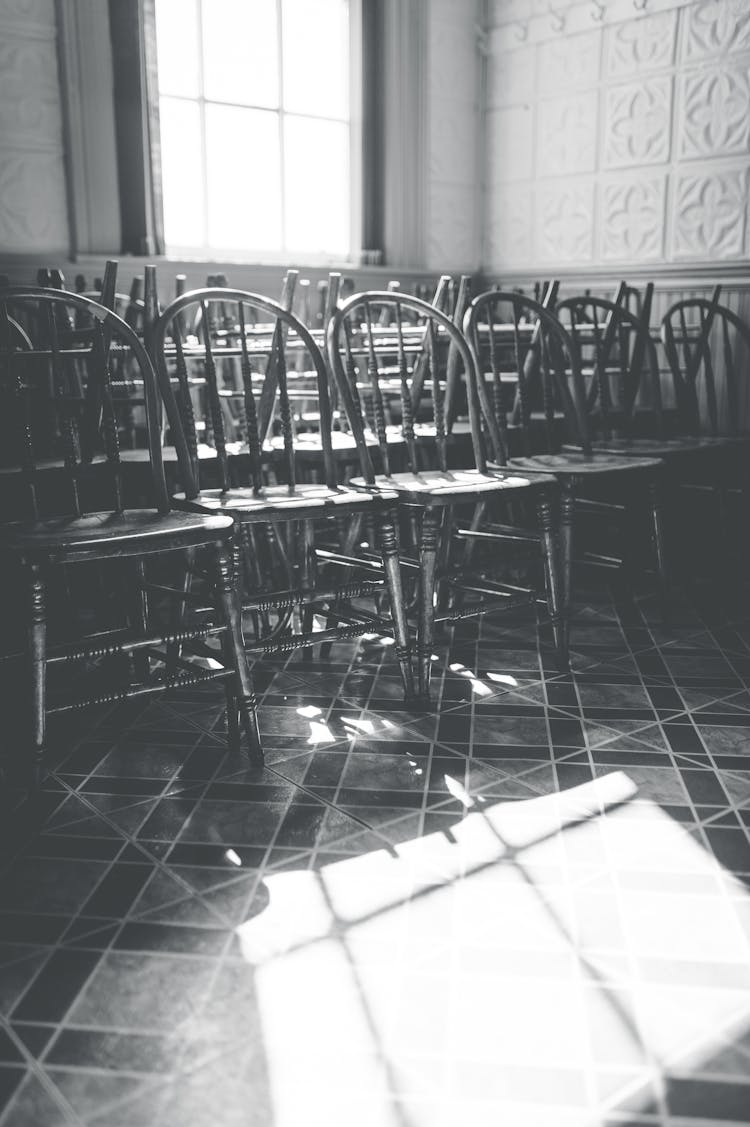 Grayscale Image Of Stack Of Chairs And Sunlight In A Room