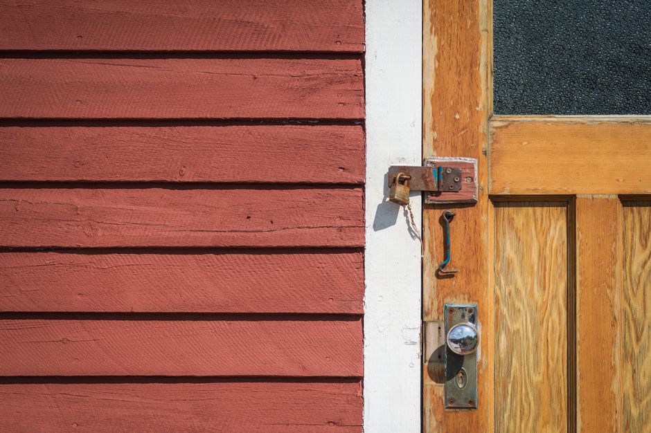 Detailed view of a wooden door and lock on a rustic red exterior wall.