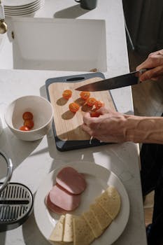 Hands slicing cherry tomatoes on a cutting board in a modern kitchen setting.